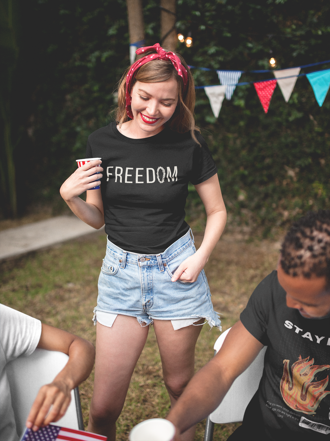 A young woman standing among friends in a black christian graphic shirt that says "Freedom" with a crown of thorns as the "o" in freedom