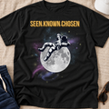 black shirt with an astronaut relaxing on the moon with a galaxy in the background and the words above 'SEEN.KNOWN,CHOSEN.'