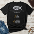 A black Christian graphic t-shirt by SeedSowerGraphics laid flat on a whitewashed wood background, styled with blue jeans, a brown leather Bible, and wooden beads. The back of the shirt features a white fish logo with 'JESUS' crossed through it, the text 'FRUIT OF THE SPIRIT TOUR', and a numbered list from 01 to 09 in gold and white.