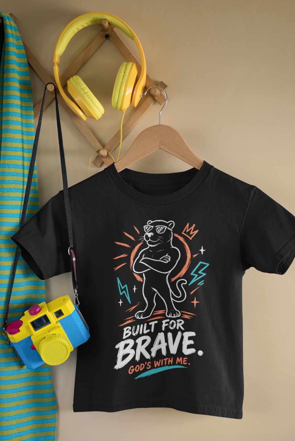 A black kids' Christianity t-shirt by SeedSowerGraphics on a wooden hanger, featuring a graphic of a panther wearing sunglasses with the text 'BUILT FOR BRAVE. GOD'S WITH ME.