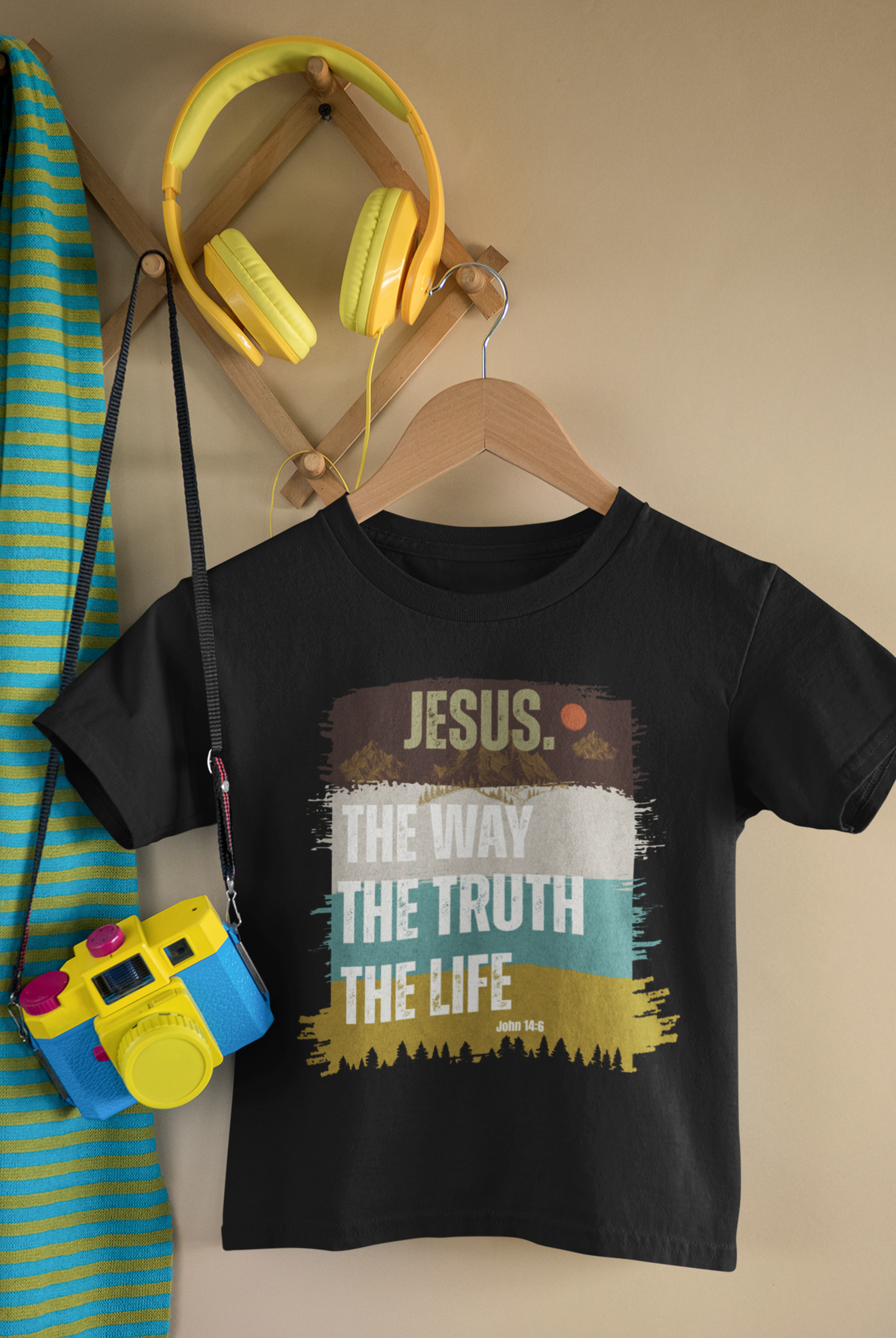 A black kids' Christian t-shirt on a wooden hanger, featuring a colorful graphic print with the text 'JESUS. THE WAY THE TRUTH THE LIFE' in a distressed paint-stroke design.