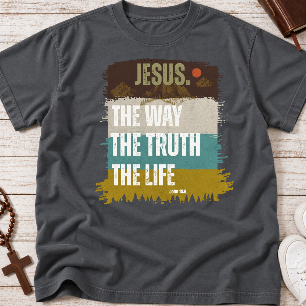 A dark gray graphic t-shirt laid flat on a light wood background, featuring a retro-style Christian design with the text 'JESUS THE WAY THE TRUTH THE LIFE' and 'JOHN 14:6' over brown, beige, teal, and mustard yellow blocks.