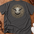 A dark gray t-shirt laid flat on a brown leather surface, showing the back with a large circular graphic of a pig's face and the text 'WHEN HE CAME TO HIS SENSES'.