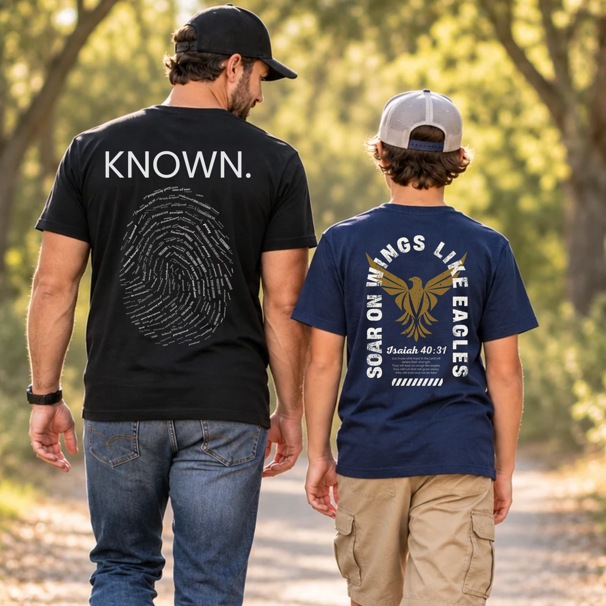 A man and a boy walking away on a tree-lined path, each wearing a Christian graphic T-shirt from SeedSowerGraphics. The man wears a black T-shirt with the word 'KNOWN and fingerprint inlaid with words of affirmation from God. The boy is wearing a navy blue Christian graphic shirt with a gold eagle emblem and words arched around it that says "soar on wings like eagles" Isaiah 40:31