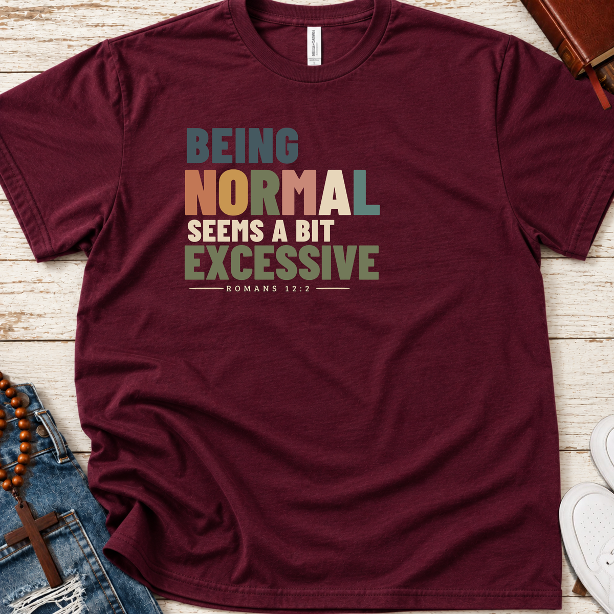 maroon shirt with colorful lettering that says 'being normal seems a bit excessive' with Romans 12:2 below it