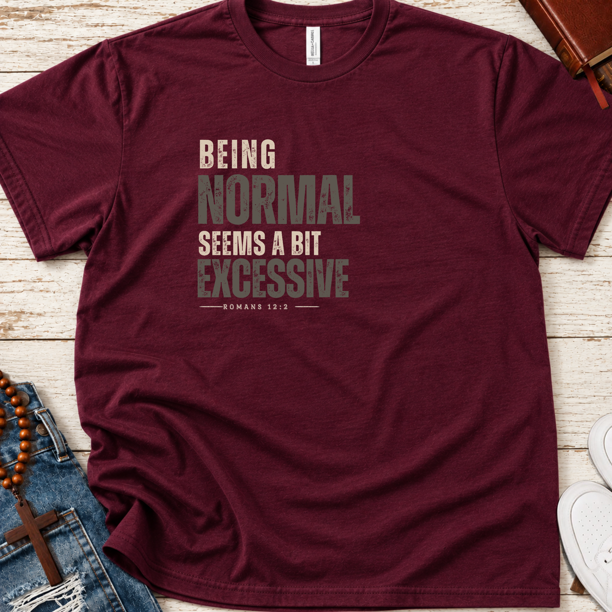 a maroon shirt that has monochrome black and gray lettering that says 'being normal seems a bit excessive' 'Romans 12:2"