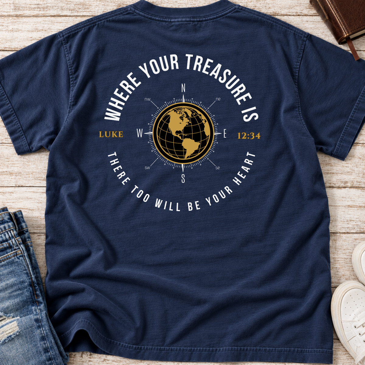 A navy blue shirt with a graphic on the back. The graphic features a gold globe compass, the text 'WHERE YOUR TREASURE IS' arched above, and 'THERE TOO WILL BE YOUR HEART' curved below, along with 'LUKE' and the time '12:34'.