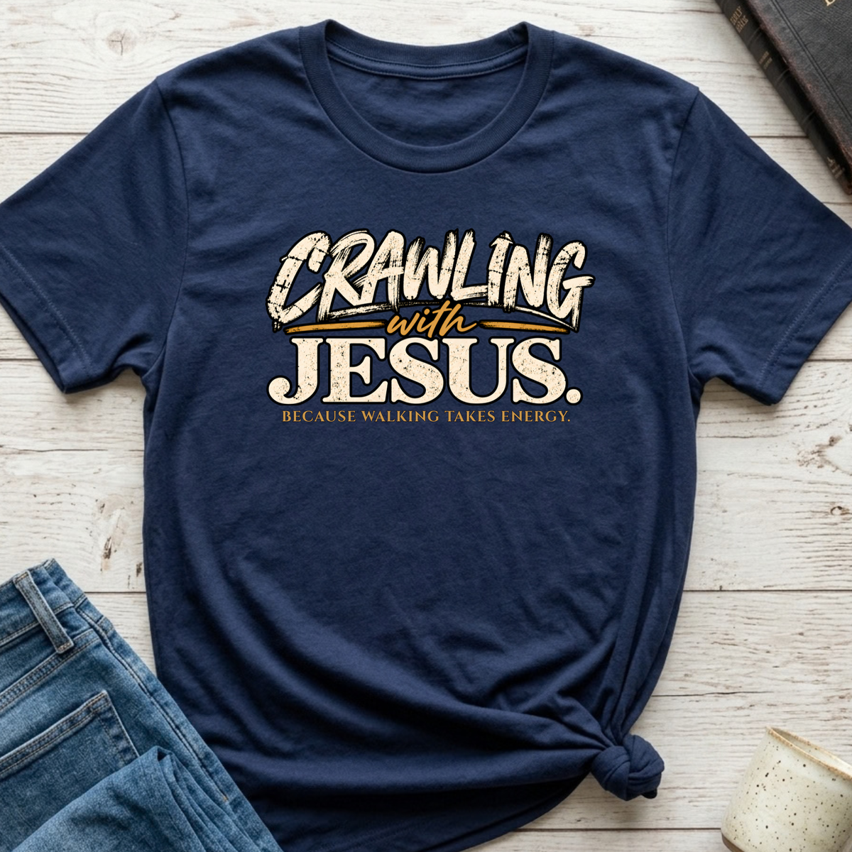 navy blue shirt laid out amongst props with the saying 'crawling with jesus' because walking takes energy.