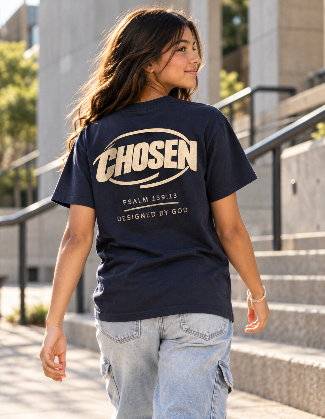 A woman wearing a navy blue t-shirt with a large cream graphic on the back that reads 'CHOSEN' and 'PSALM 139:13 DESIGNED BY GOD', walking outdoors on concrete stairs.