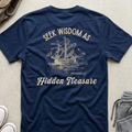 A navy blue t-shirt laid flat on a light concrete surface, featuring a cream-colored graphic of a sailing ship and the text 'SEEK WISDOM AS Hidden Treasure PROVERBS 2:4'.