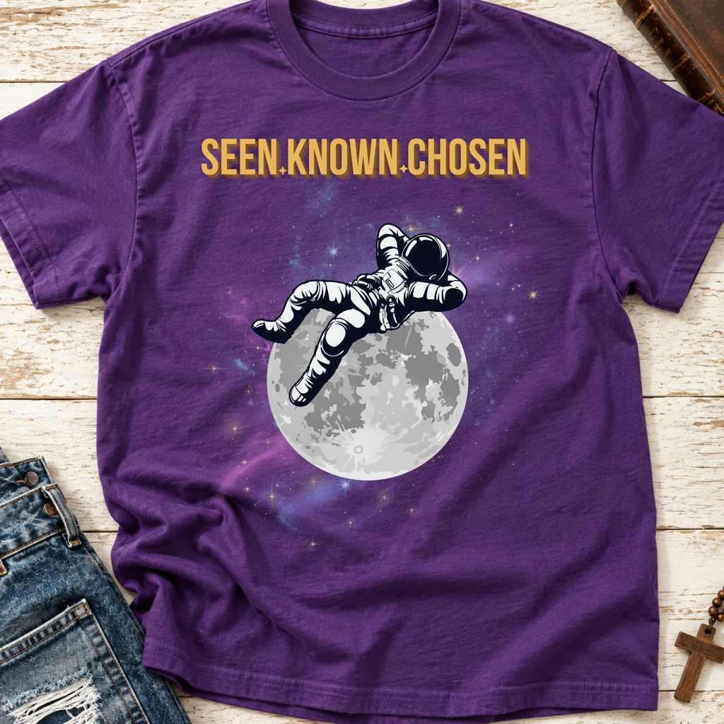 Purple shirt with an astronaut relaxing on the moon with a galaxy in the background and the words above 'SEEN.KNOWN,CHOSEN.'