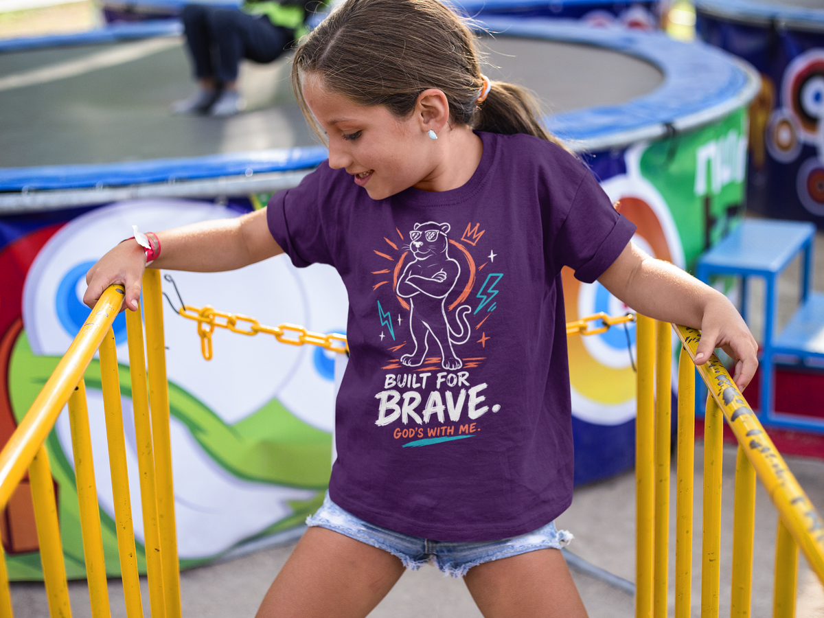 A young girl wearing a purple Christian graphic t-shirt by SeedSowerGraphics with a cartoon jaguar and the text 'BUILT FOR BRAVE. GOES WITH ME.