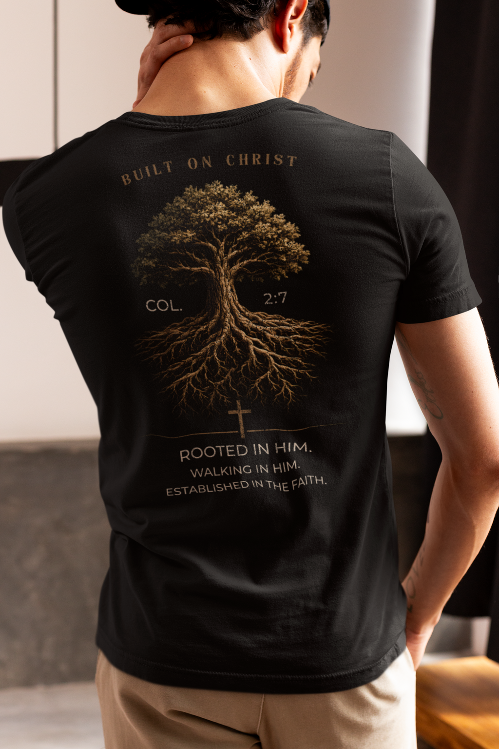 Person wearing a blackChristian graphic t-shirt with a tree on the back with the words 'Built on Christ' 'Rooted in Him' standing indoors.