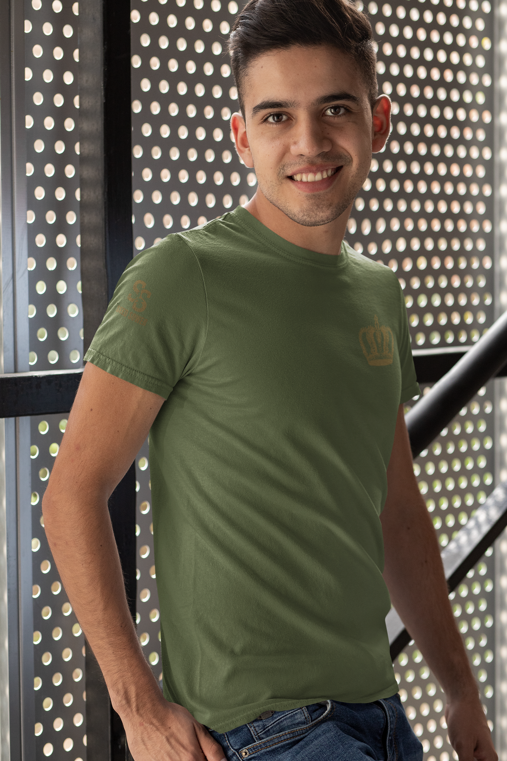 A man wearing an olive green crewneck Christian Redeemed t-shirt by SeedSowerGraphics with a small gold crown logo on the left chest, standing in front of a perforated metal screen.