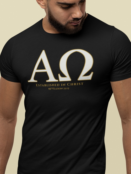 A man wearing a black Christian faith t-shirt with a large white Greek letter design (Alpha Omega) and the text 'ESTABLISHED IN CHRIST REVELATION 22:13' printed on the chest, set against a solid beige background.
