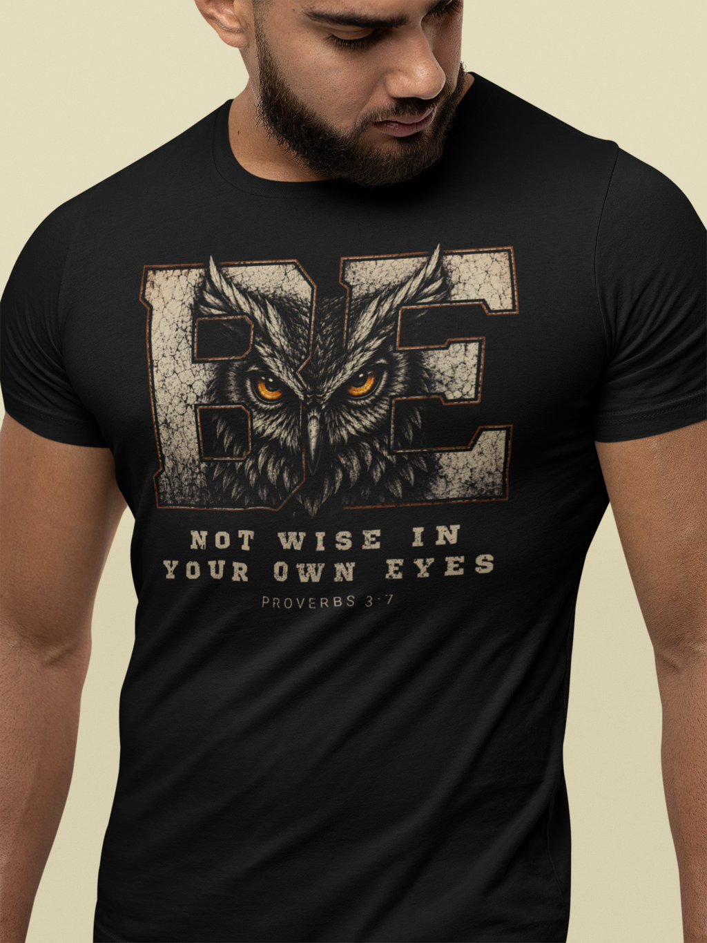 A man wearing a black short-sleeve Christian graphic t-shirt with a distressed owl design and the text 'BE NOT WISE IN YOUR OWN EYES Proverbs 3:7' on a light beige background.