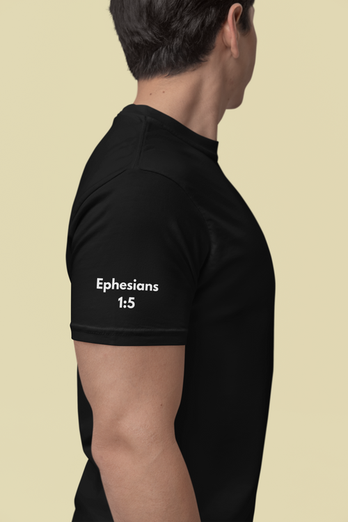 A man shown from the side wearing a black Christian faith based t-shirt with the text 'Ephesians 1:5' printed in white on the left sleeve, against a solid light beige background.