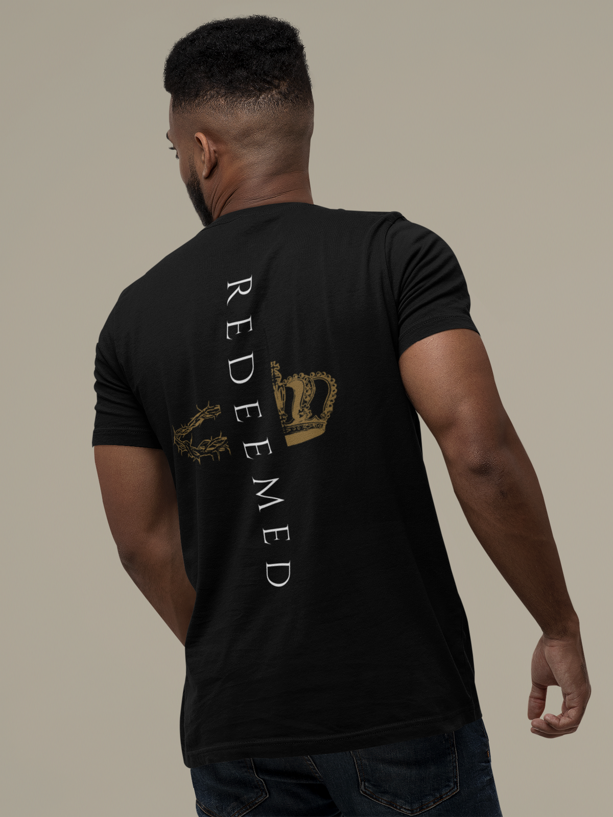 A man shown from the back wearing a black Christian t-shirt by SeedSowerGraphics with a graphic design on the back. The design features the word 'Redeemed' printed vertically in white, alongside a gold crown and a gold circular emblem.