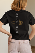 A woman shown from the back wearing a black short-sleeve Christian graphic T-shirt from SeedSowerGraphics with vertical white 'Redeemed' text and a distressed gold crown graphic, paired with light pink jeans.