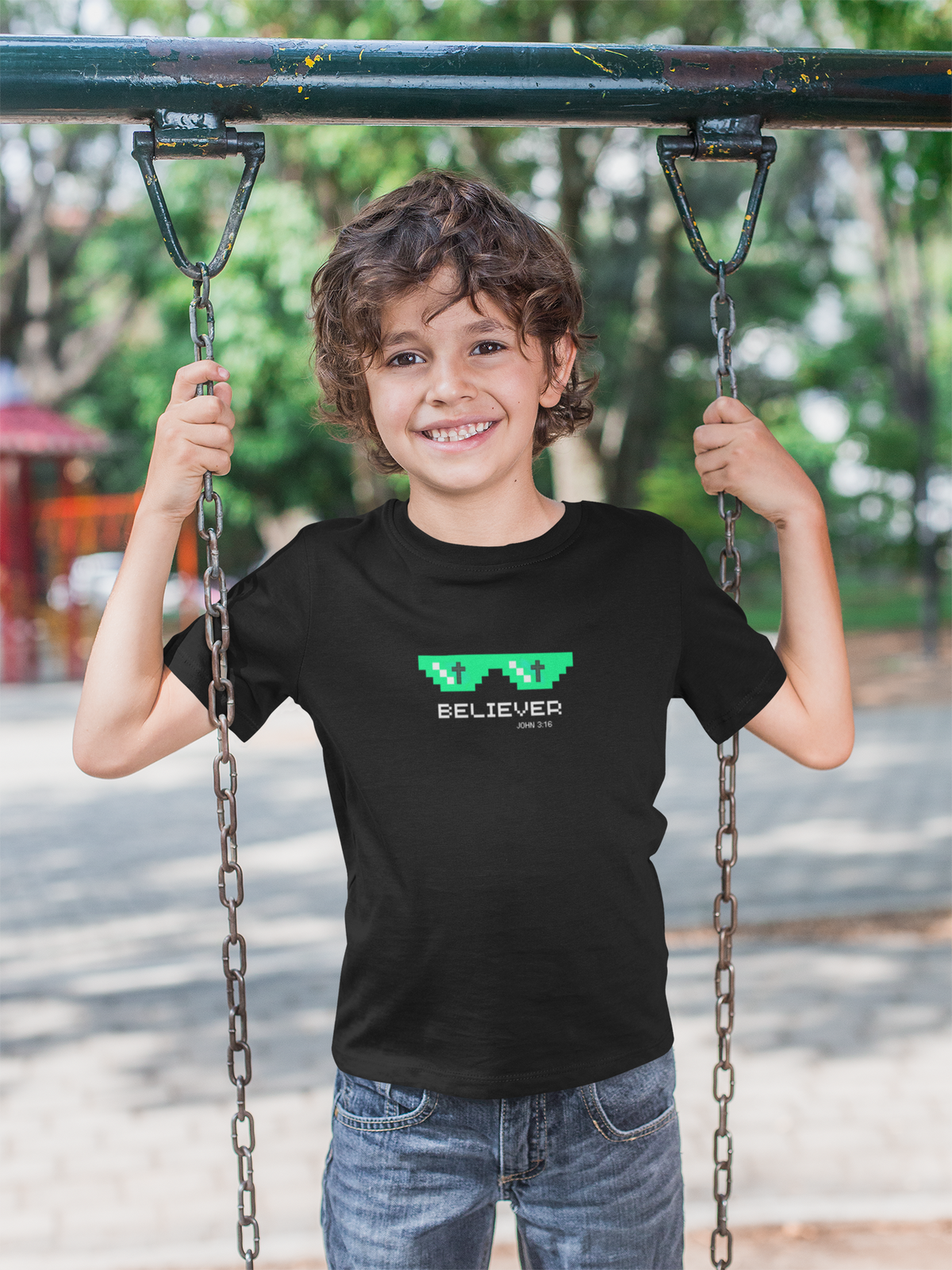 Child wearing a black t-shirt with 'Believer' text on a swing set.