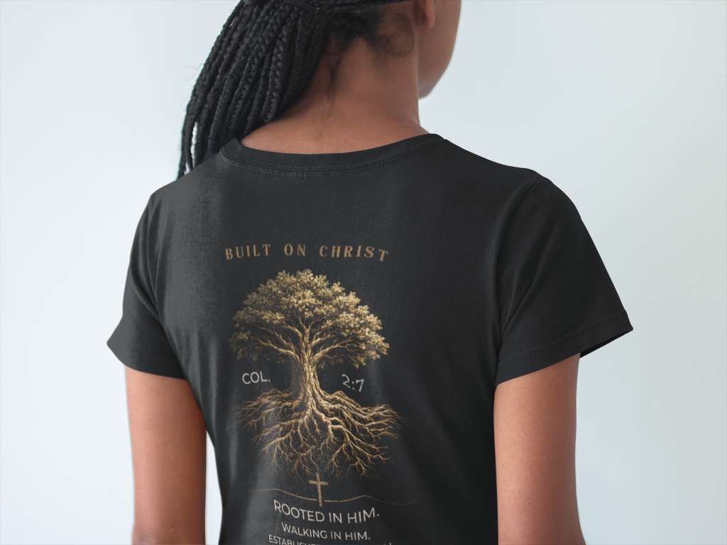 A person shown from the back wearing a black short-sleeve Christian graphic T-shirt with a large gold-toned graphic of a tree and text reading 'BUILT ON CHRIST' and 'ROOTED IN HIM'.