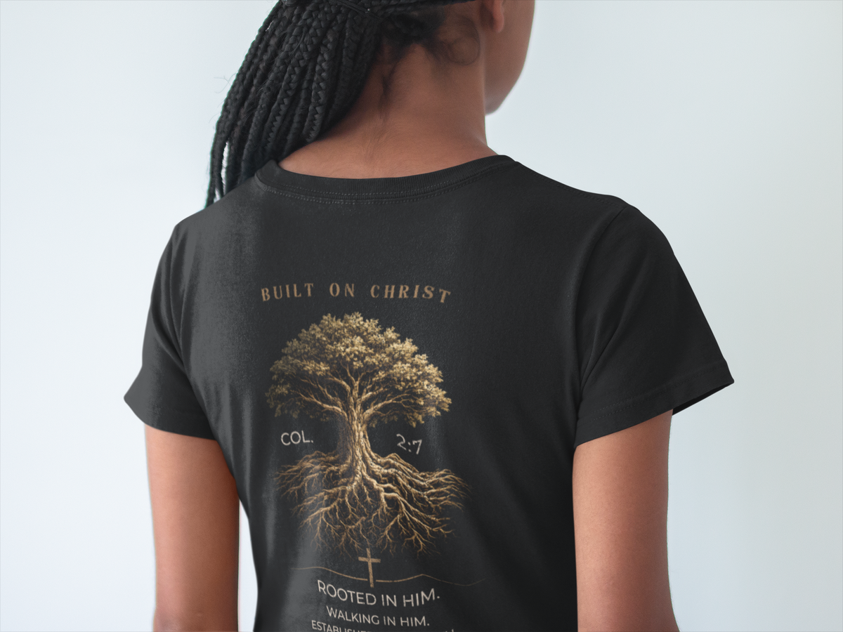 A person shown from the back wearing a black short-sleeve Christian graphic T-shirt with a large gold-toned graphic of a tree and text reading 'BUILT ON CHRIST' and 'ROOTED IN HIM'.