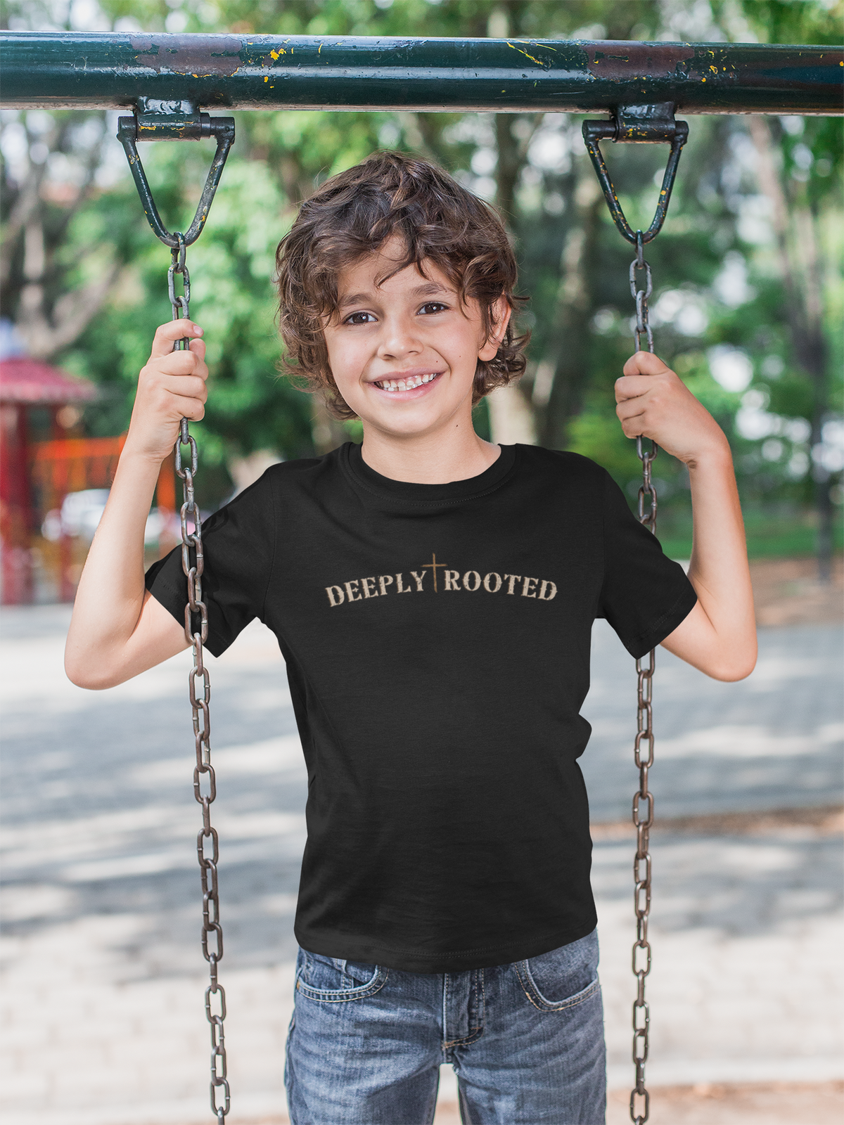 Child wearing a black Christian graphic t-shirt with 'Deeply Rooted' text on a swing set.
