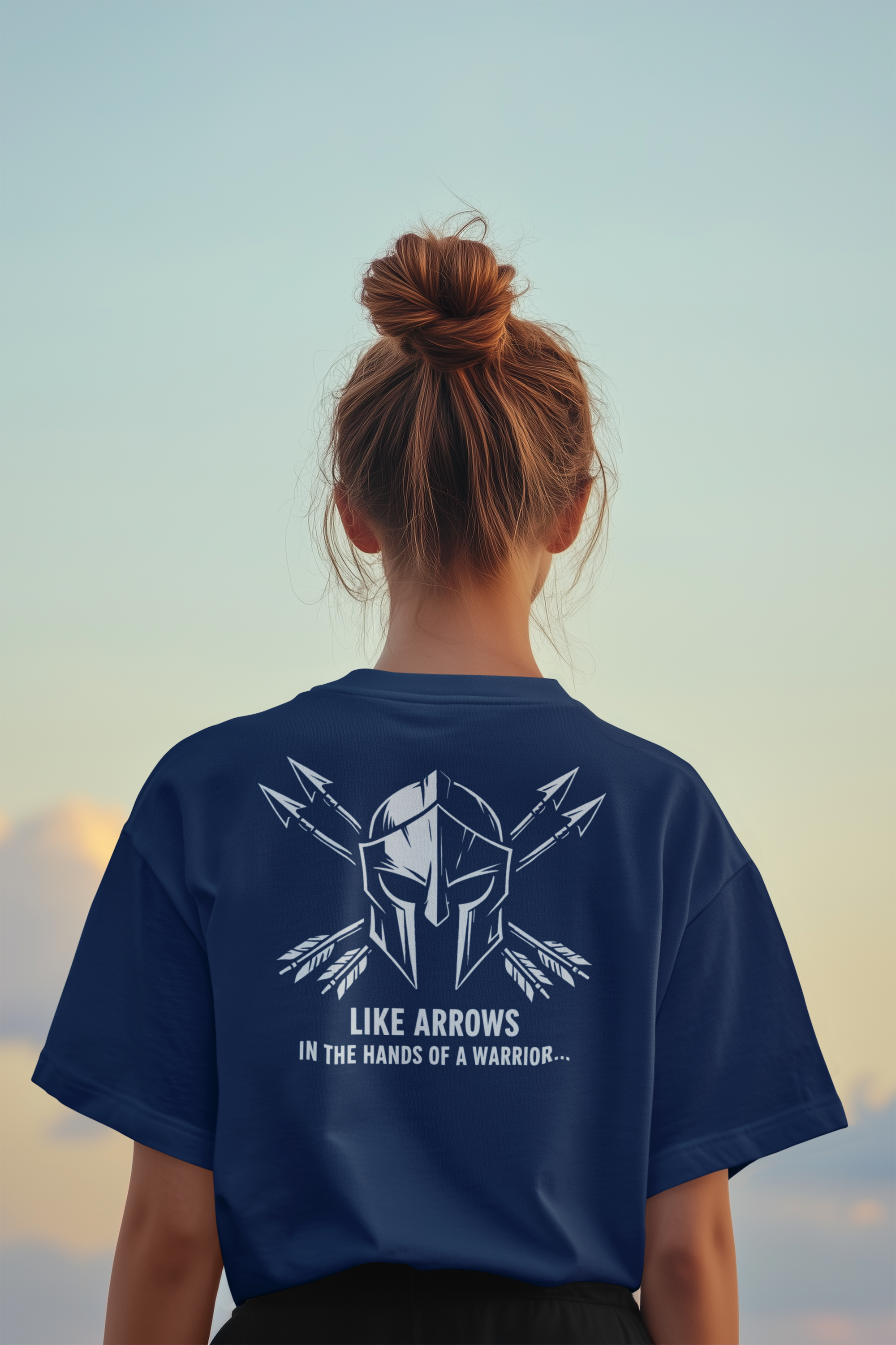 A girl viewed from behind wearing a navy blue Bible verse t-shirt with a white graphic of a Spartan helmet and crossed arrows, with the text 'LIKE ARROWS IN THE HANDS OF A WARRIOR.