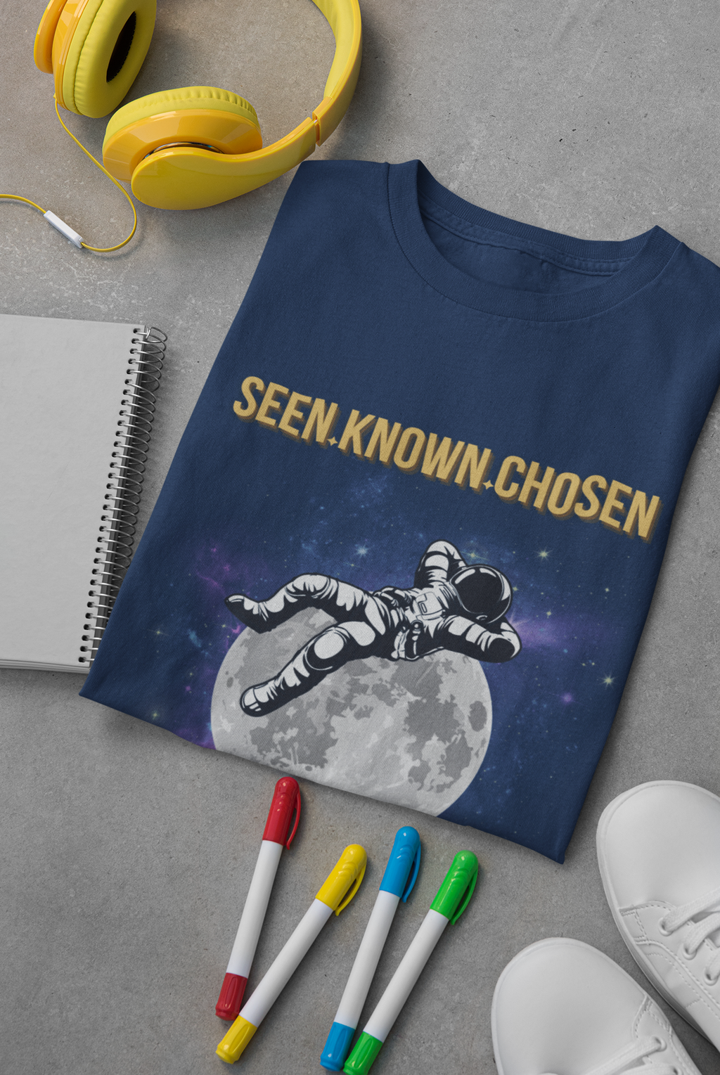 A navy blue Christian graphic t-shirt featuring an astronaut floating in space above a moon, with the text 'SEEN. KNOWN.CHOSEN'