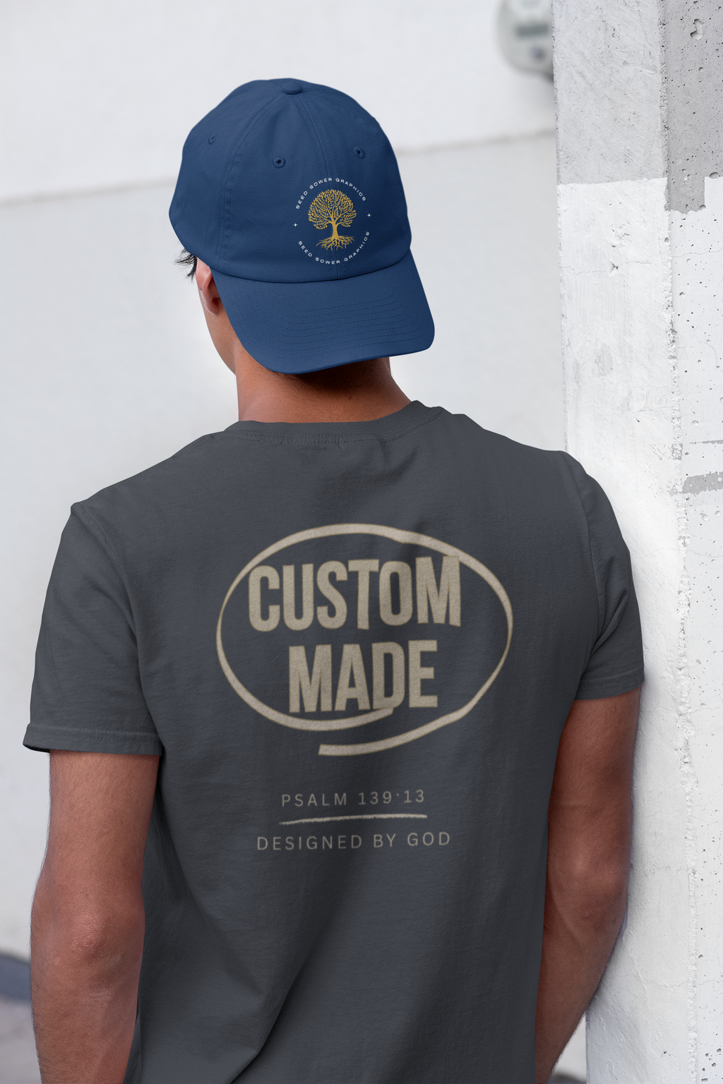 The back view of a young man wearing a gray Christian graphic tee with the word 'Custom Made' real big centered along the back encircled by a cream circle. Beneath the word are smaller words reading, 'Psalm 139:13' and 'Designed by God'.