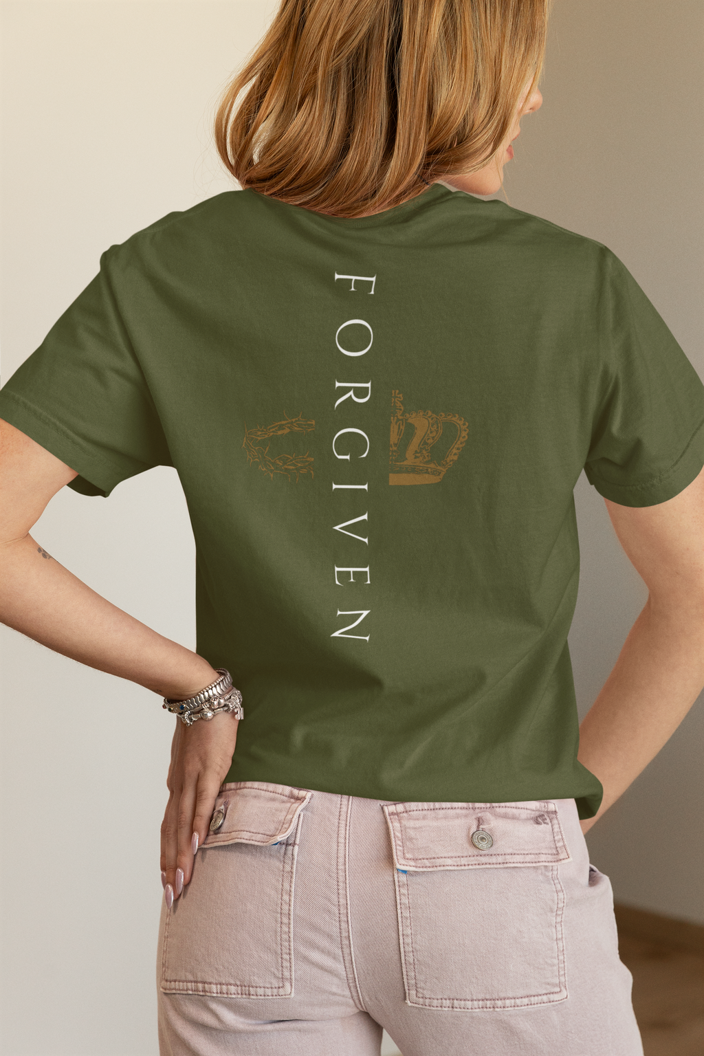 Woman wearing a green shirt with the word "Forgiven" lined vertically down her back with gold graphics of  crown and crown of thorns on either side of the word.