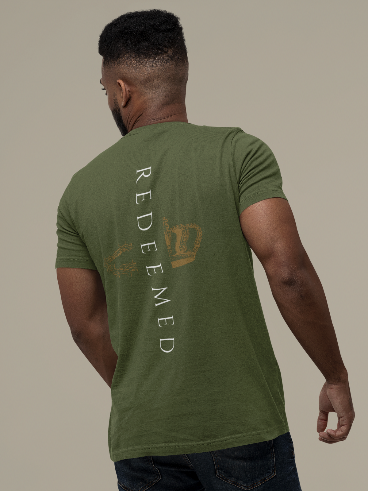 A man shown from behind wearing an olive green Christian graphic t-shirt by SeedSowerGraphics with a vertical graphic on the back. The graphic features the word 'Redeemed' in white vertical letters next to a distressed gold crown and a gold peace sign.