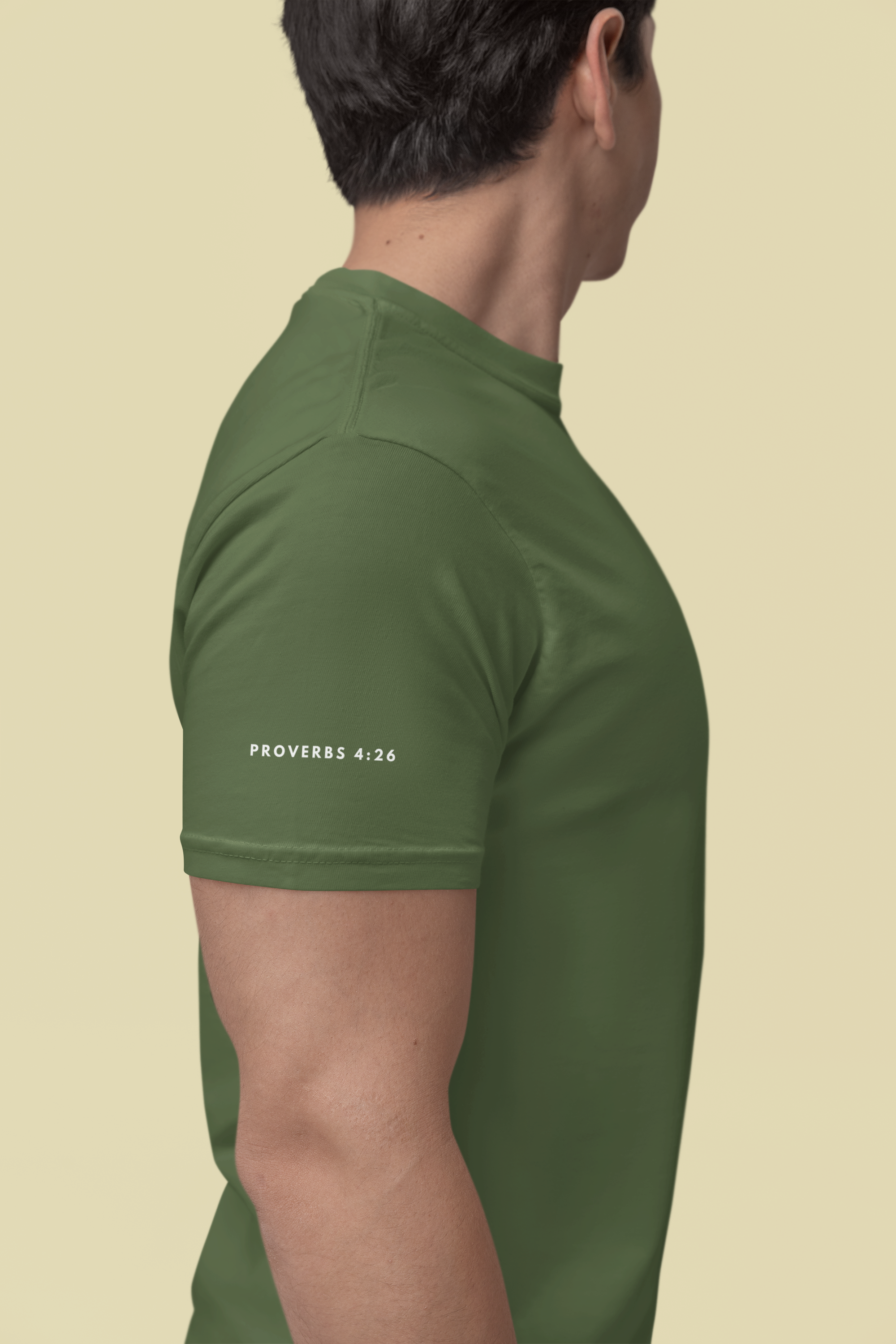 A man shown from the side wearing a fitted short-sleeve Christian Bible verse t-shirt in olive green. The shirt features the text 'PROVERBS 4:26' printed in white on the left sleeve.