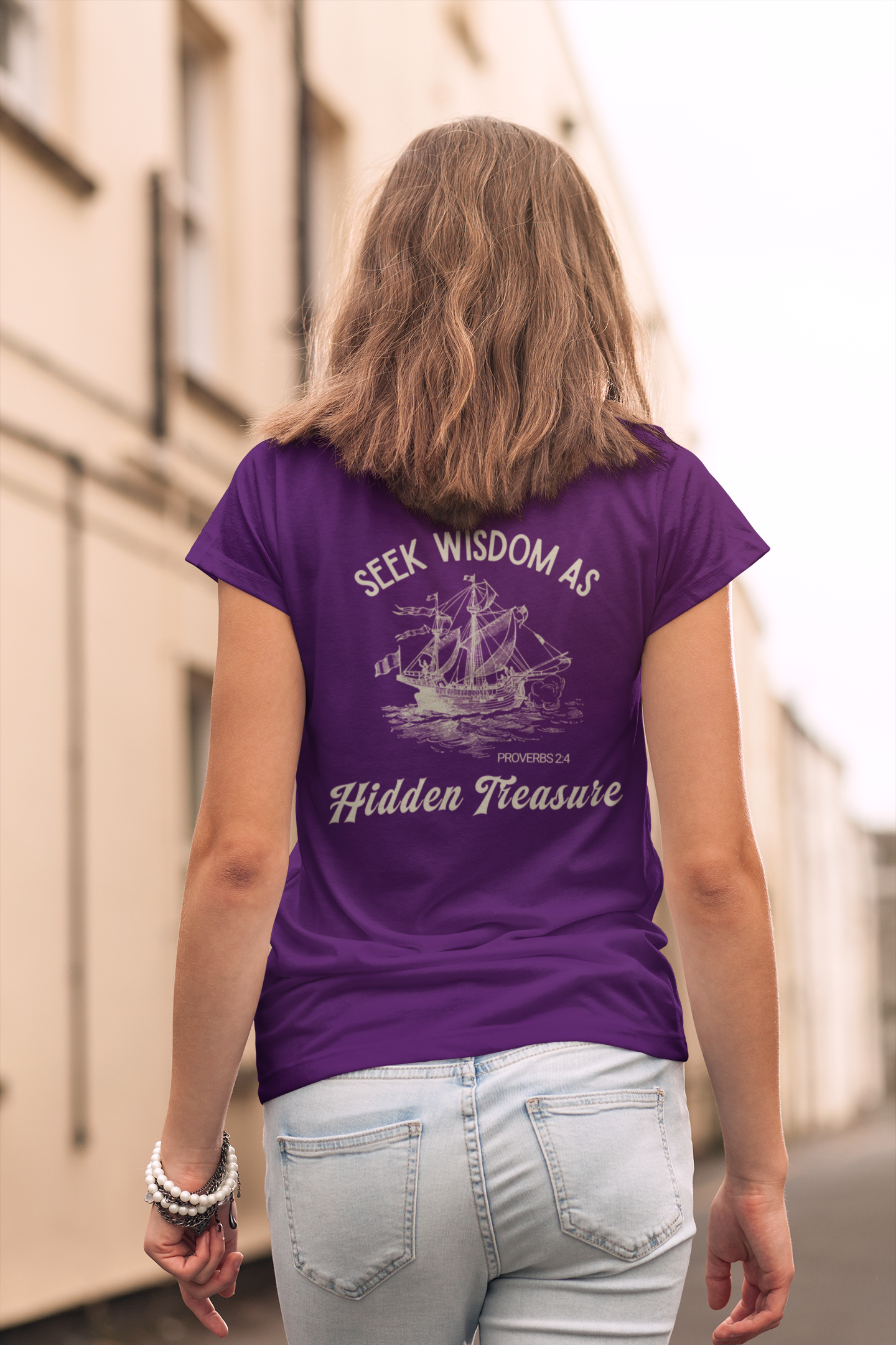 A girl viewed from behind wearing a purple short-sleeve Bible verse T-shirt with a cream graphic print of a sailing ship and the text 'SEEK WISDOM AS Hidden Treasure'. 