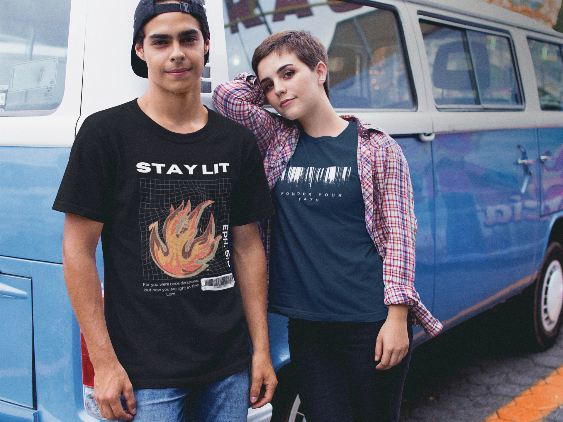 Two people standing in front of a blue van, one wearing a black Christian graphic 'Stay Lit' t-shirt with a flame design, and the other wearing a blue Christian faith shirt that says 'Ponder Your Path'