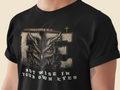 A close-up of a person wearing a black Christian graphic t-shirt. The shirt features a large distressed graphic of an owl's face inside the word 'BE', with 'PROVERBS 3:7' above and 'NOT WISE IN YOUR OWN EYES' below in white text.