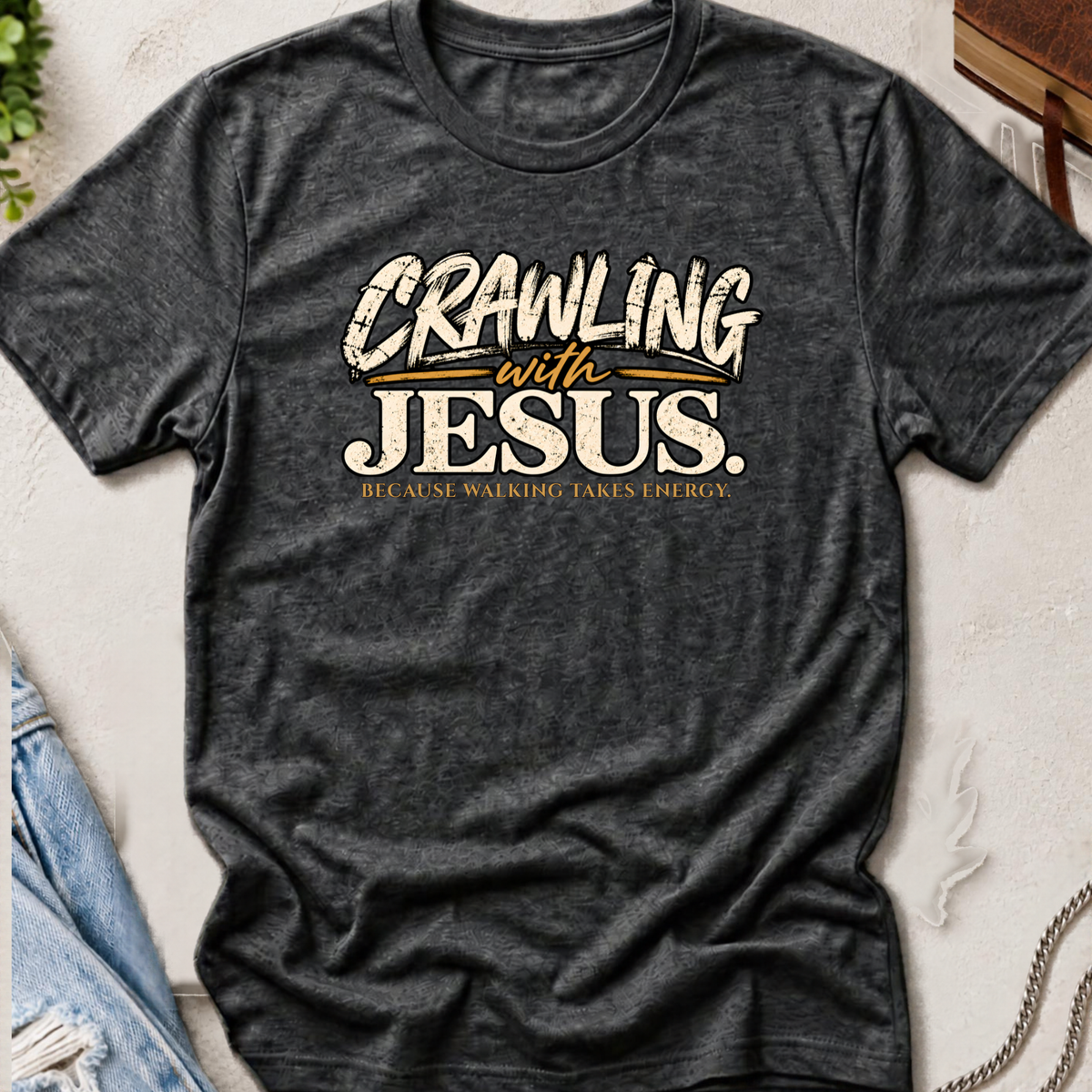 heather grey Christian t-shirt by SeedSowerGraphics laid out amongst props with the saying 'crawling with jesus' because walking takes energy.