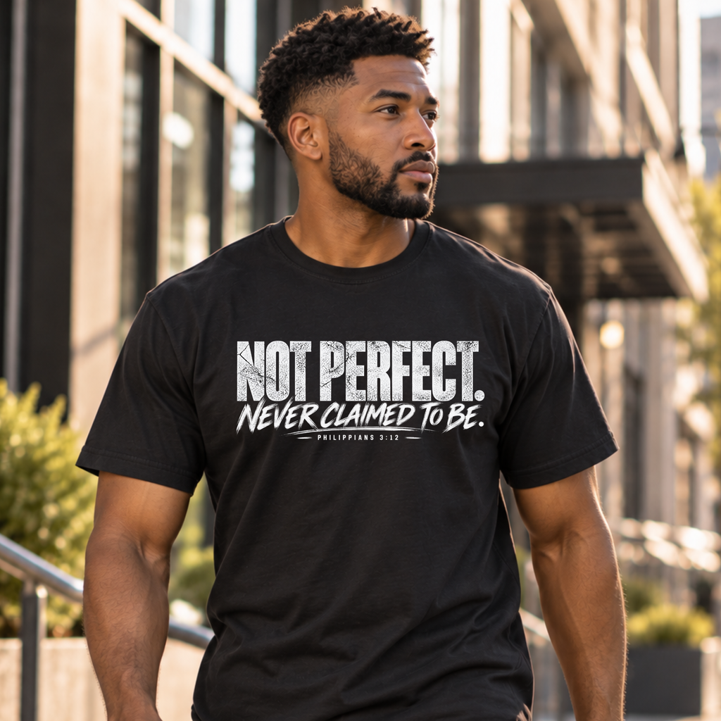A man wearing a black graphic t-shirt with the text 'NOT PERFECT. NEVER CLAIMED TO BE.