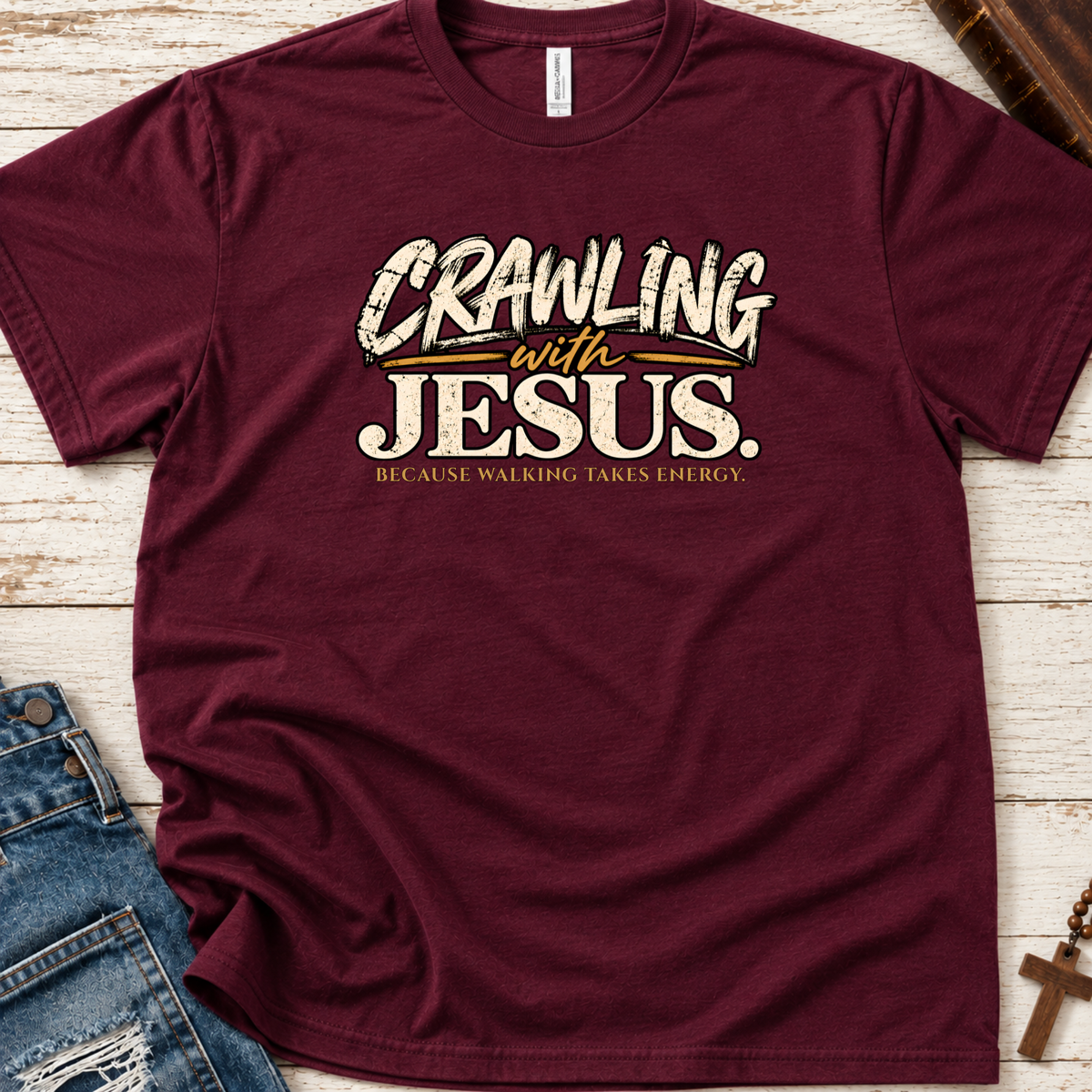 maroon Christian t-shirt by SeedSowerGraphics laid out amongst props with the saying 'crawling with jesus' because walking takes energy.