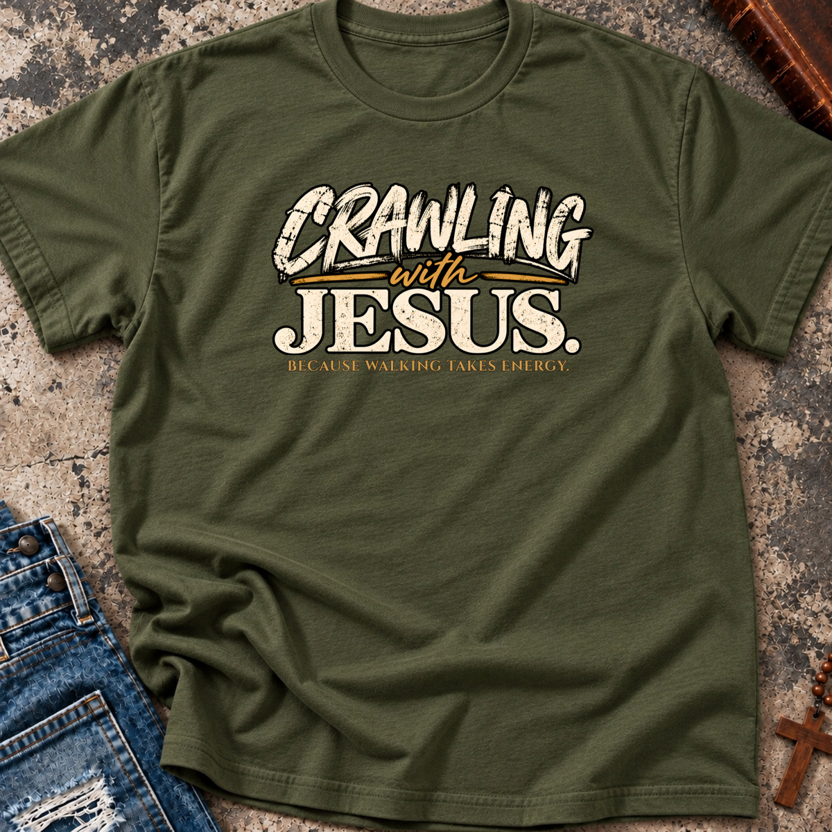 military green Christian t-shirt by SeedSowerGraphics laid out amongst props with the saying 'crawling with jesus' because walking takes energy.