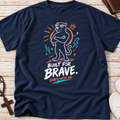 A navy blue graphic t-shirt laid flat on a light wood background. The shirt features a stylized panther wearing sunglasses with its arms crossed, surrounded by orange and teal lightning bolts and stars, with the text 'BUILT FOR BRAVE.