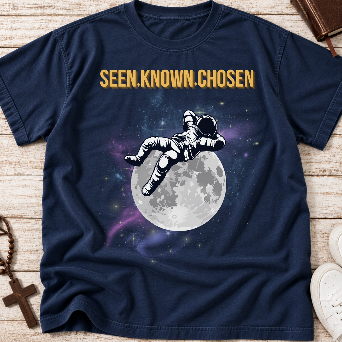 Navy blue shirt with an astronaut relaxing on the moon with a galaxy in the background and the words above 'SEEN.KNOWN,CHOSEN.'