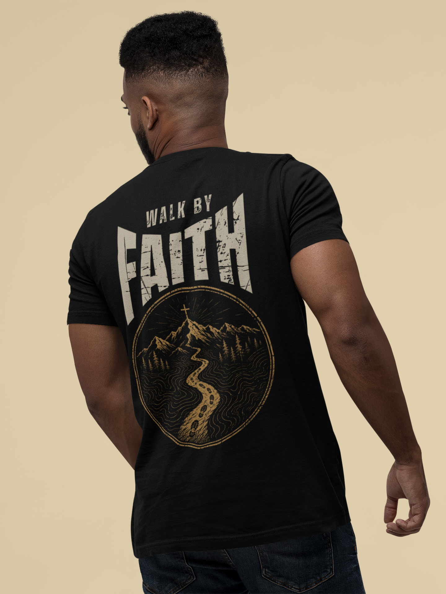 A man shown from the back wearing a black Christian graphic t-shirt with a large graphic on the back. The graphic features the words 'WALK BY FAITH' in distressed cream lettering above a circular gold and white topographic map design of a mountain and river.